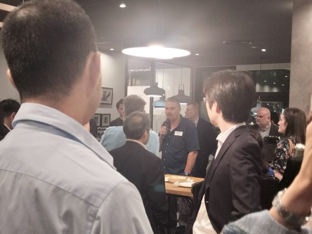 Jason Ball attends the business networking event BlendTokyo. He gives an address to a crowd with a microphone. 